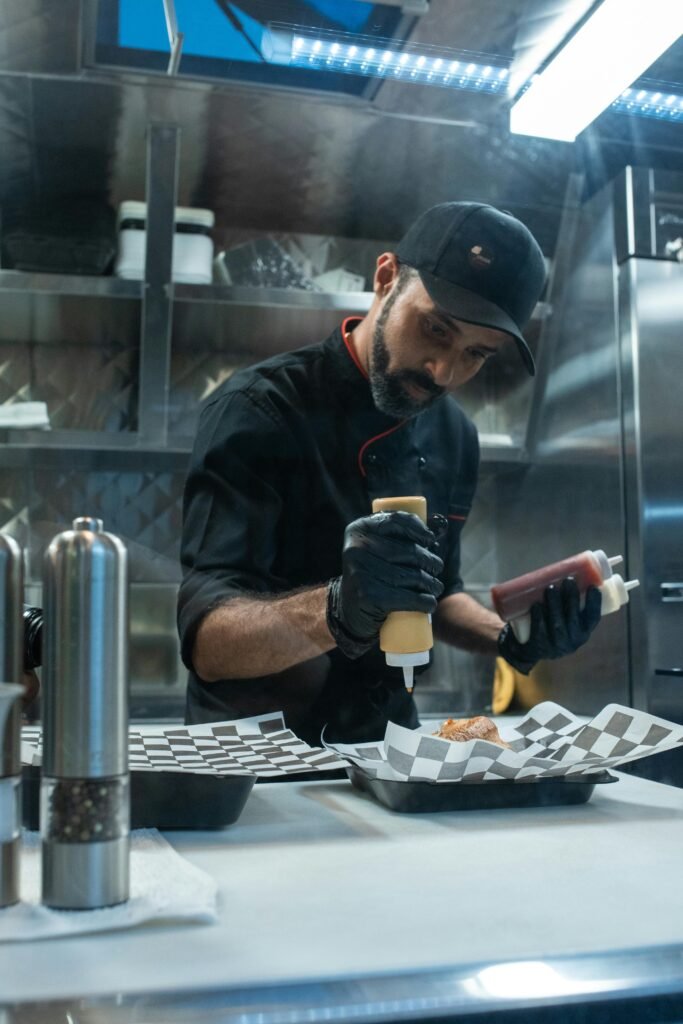 A chef skillfully adding condiments to a dish in a professional kitchen setting.