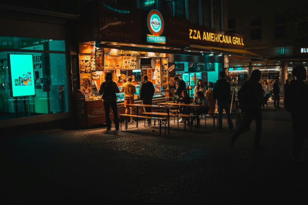 A lively street scene at night with people gathering around a pizza restaurant.